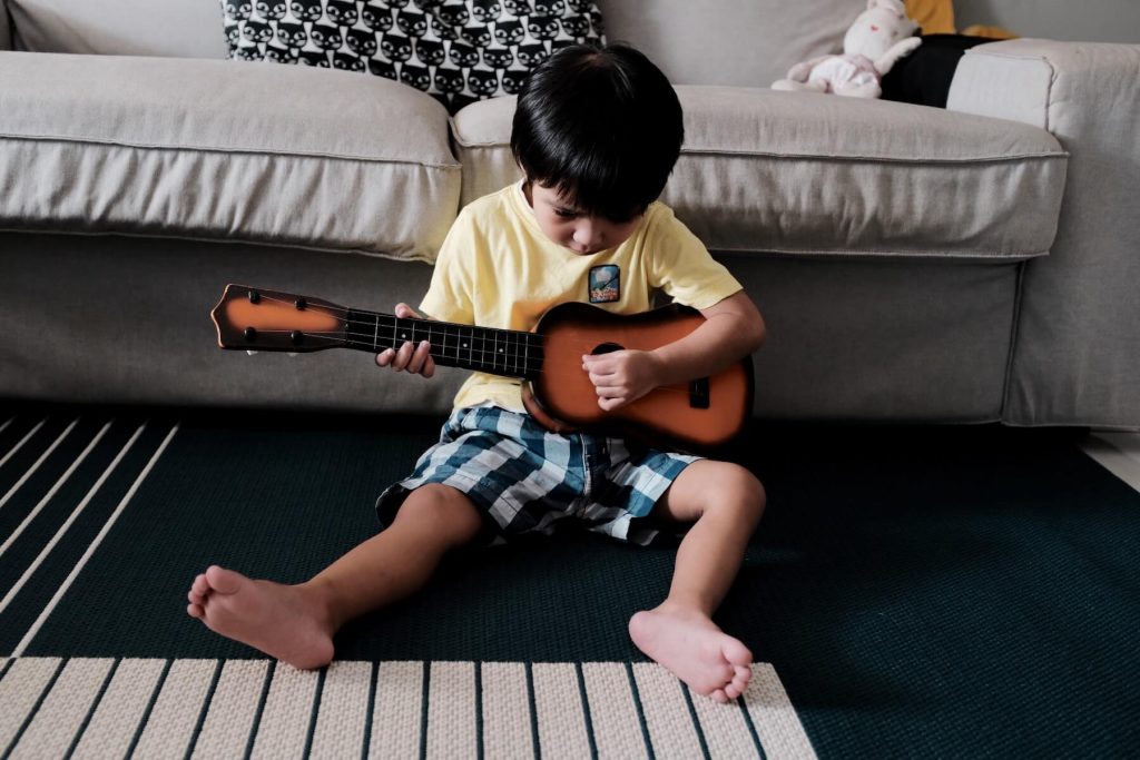 little boy playing the ukulele at home