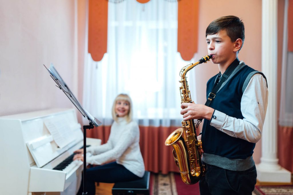 boy learning how to play saxophone with teacher