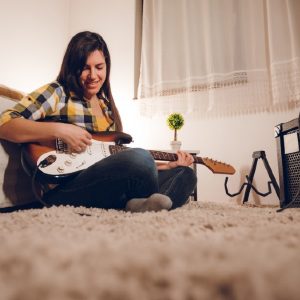 A female guitarist plays a guitar plugged into a combo guitar amp.