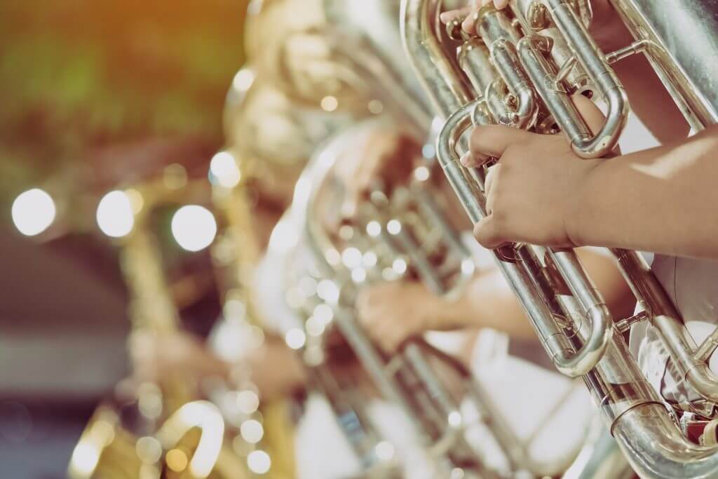 Male student with friends blow the euphonium with the band for performance on stage at night