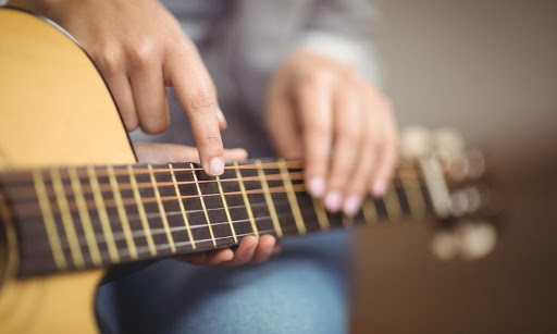 A student takes a guitar lesson from an instructor who demonstrates finger placement.