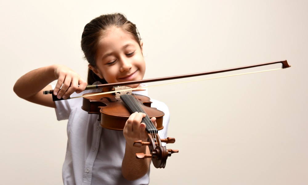 A young girl draws a bow across a violin during strings lessons