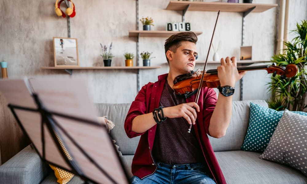 Young male violinist practicing music at home.